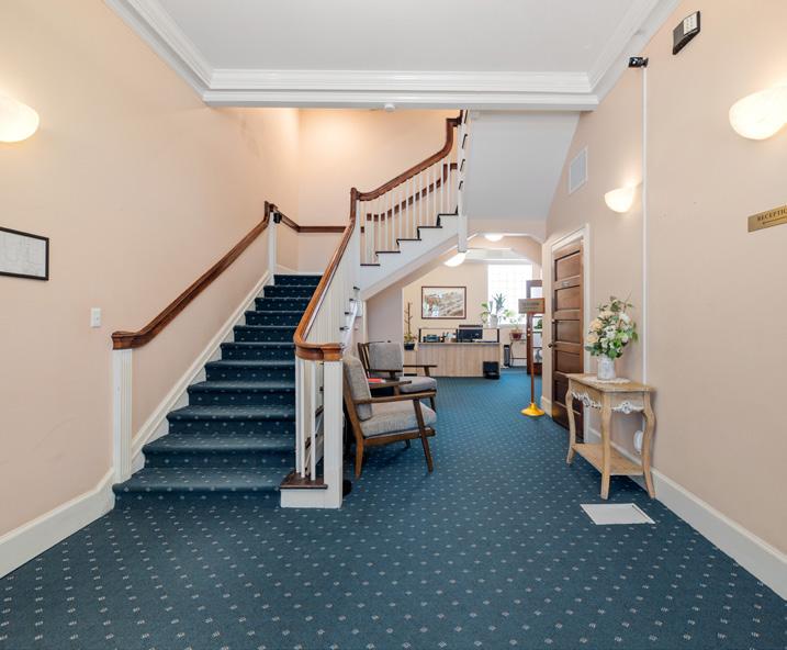Lobby with blue carpet, wooden staircase, two armchairs, and a reception desk in the back.