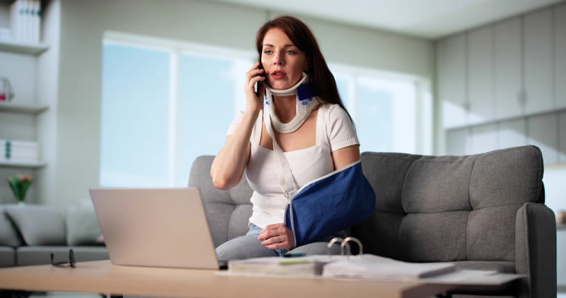 A woman in a neck brace and arm sling on the phone with her personal injury attorney.