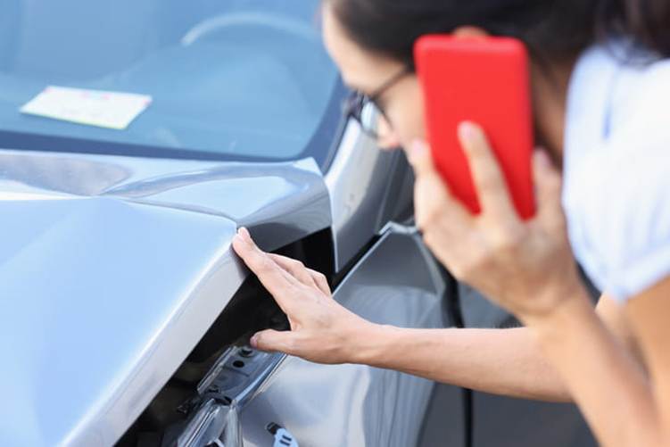 A person on their phone and inspecting the damage to their vehicle after being in a hit-and-run accident.